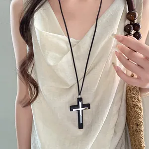 Vista dettagliata della collana con pendente a croce nera e argento su modella in abito crema