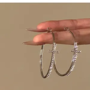 Detailed view of elegant silver-colored rhinestone cross hoop earrings held by hand