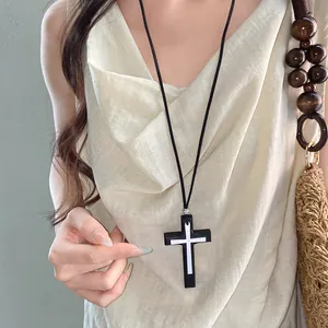 Primo piano di una collana vintage con croce nera indossata su un abito in lino
