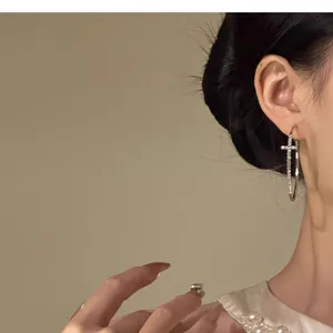 Detailed view of a silver hoop earring featuring a delicate diamond-set cross pendant.