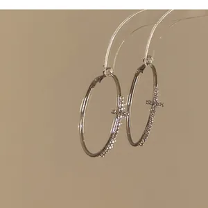 Close-up detail of silver hoop earrings with rhinestone cross design
