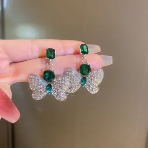 Detailed view of silver butterfly earrings featuring emerald green gemstones and rhinestones