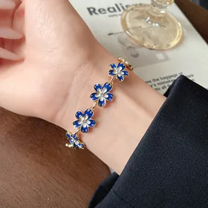 Primo piano del braccialetto floreale smaltato blu e bianco al polso di una donna asiatica.