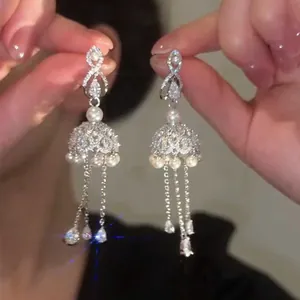 Close-up of sparkling silver bow earrings with pearls and long diamond-set tassels