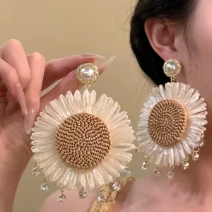 Detail view of oversized bohemian woven sunflower earrings with pearls and crystals
