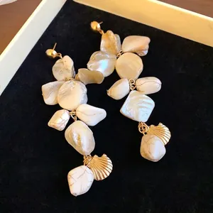 Eleganti orecchini pendenti a conchiglia irregolari dorati su vassoio in velluto nero