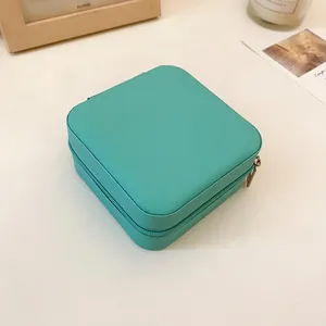 Primer plano de un joyero portátil de cuero verde azulado con cremallera y textura.