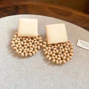 Detailed view of beige geometric stud earrings with woven beaded circular drops