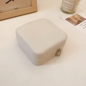 Detalle de un joyero cuadrado minimalista de cuero crema con cierre de cremallera