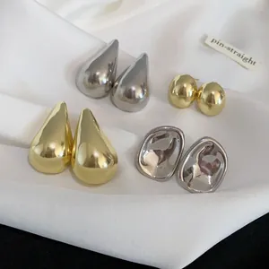 Colección detallada de pendientes metálicos geométricos y de gota sobre satén blanco
