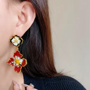 Close-up of vintage floral drop earrings with red enamel and rhinestone details.