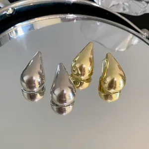 Primer plano de pendientes minimalistas de gota de agua en oro y plata sobre un espejo