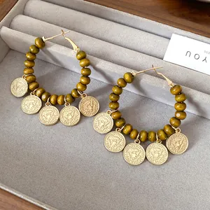 Close-up of boho hoop earrings with green wooden beads and eagle coin charms on grey tray