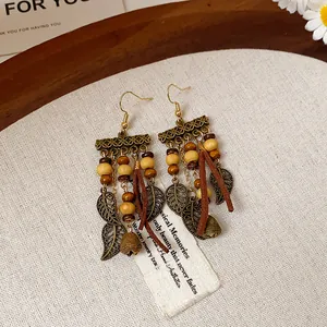 Close-up of boho vintage earrings with metal leaves, wood beads, and leather tassels.