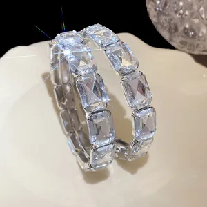Close-up of exaggerated hoop earrings with rectangular clear crystals and silver pins.