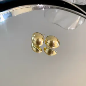 Primer plano de pendientes de botón minimalistas dorados con forma de haba en espejo.
