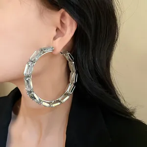Detailed macro view of large silver hoop earrings with rectangular crystal stones on model