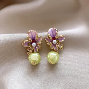 Close-up detail of purple enamel flower earrings with pearls on silk fabric