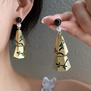 Close-up of retro Chinese style earrings with pearl and golden geometric pendants.