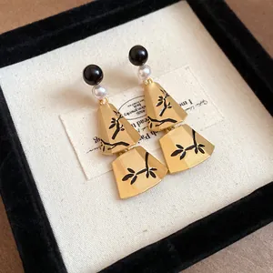 Close-up of retro Chinese style earrings with pearls and black branch patterns on gold pendants.