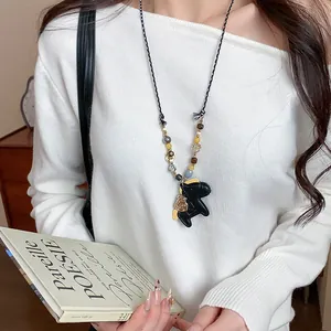 Close-up of long necklace with leather horse pendant and wooden beads on white sweater.