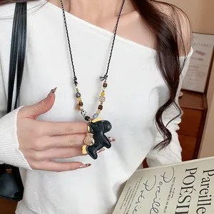 Detail of a leather horse pendant necklace with wooden and stone beads worn by a model