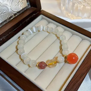 Detail of ethnic style white beaded bracelet with an orange peach pendant in a gift box