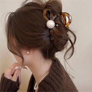 Detail view of a stylish tortoise shell hair claw clip with a large pearl on a bun