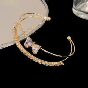 Macro detail of gold-tone double-row cuff bracelet with zircon bow and crystal inlay.
