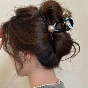 Close-up of a stylish black wave hair claw clip with a large pearl on a hairstyle.