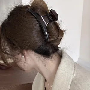 Elegant brown hair claw clip with pearl accents shown in a stylish updo hairstyle.