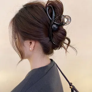 Close-up of a wavy black hair claw clip used to secure a bun on an Asian model.