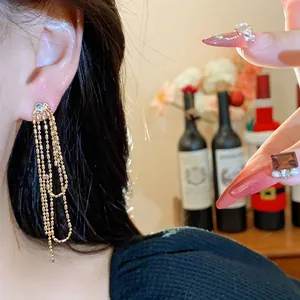 Eleganti orecchini lunghi a nappa dorata con zirconi indossati sull'orecchio di una modella