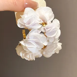 Macro view of white chiffon fabric flower C-shaped earrings with elegant gold accents
