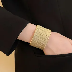Detalle de un brazalete ancho dorado envuelto en alambre en la muñeca