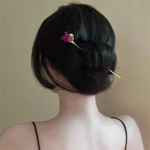 Détail d'un pic à cheveux élégant avec rose séchée et perle dans un chignon noir.