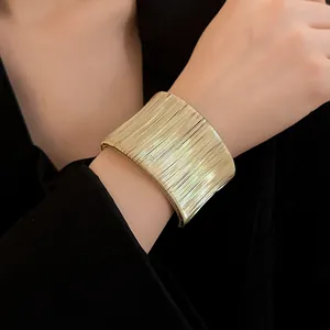 Primer plano de un brazalete ancho de alambre dorado enrollado minimalista en la muñeca