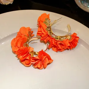 Close-up of orange chiffon flower C-shaped earrings with delicate gold metal accents
