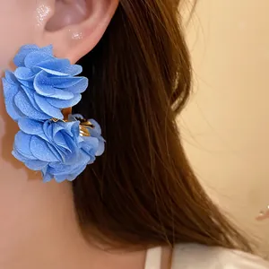 Macro view of blue chiffon fabric flower C-shaped stud earrings with silver needle detail