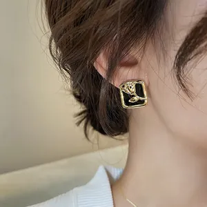 Close-up of a vintage black square stud earring with a gold rose on a woman's ear