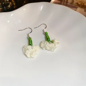 Detail view of handmade white crochet flower earrings with green stems on a white plate