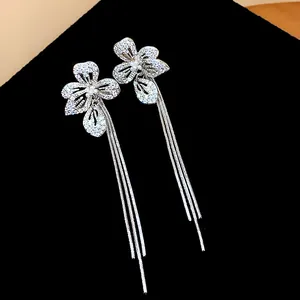 Dettaglio ravvicinato di eleganti orecchini floreali con zirconi e lunghe nappe metalliche.
