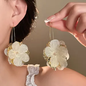 Close-up detail of white hollow petal flower drop earrings with golden accents worn by model