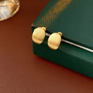 Close-up of minimalist matte gold geometric oval stud earrings on green box