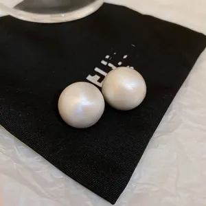 Macro view of large white pearl stud earrings on a black fabric background.