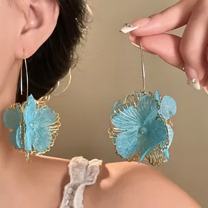 Detailed macro view of light blue fabric flower drop earrings with hollow golden metalwork
