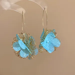 Close-up of elegant blue fabric flower earrings with gold hollow design details.