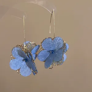 Close-up of blue mesh flower earrings with gold hollow petal details and long wire hooks.