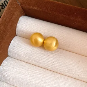 Detailed close-up of minimalist golden matte ball stud earrings displayed in a jewelry box