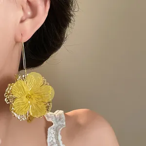 Close-up of vibrant yellow hollow flower drop earring worn by model for elegant styling.
